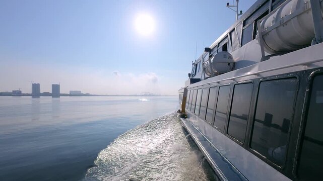 A real-time 60fps side view of a ferry, showing water wake and sun reflection with a distant city skyline on the horizon.