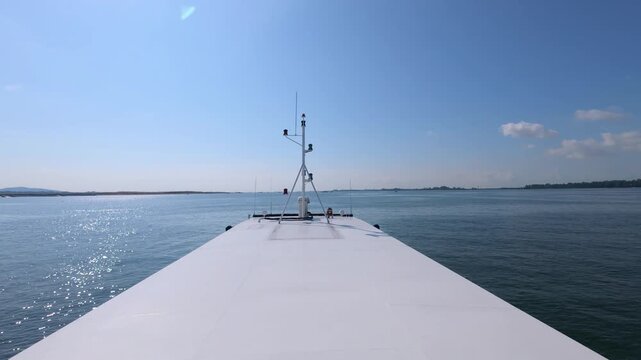 Point-of-view shot from a moving ship deck showing a long white bow and a distant urban horizon along a major shipping lane in the Singapore Strait.