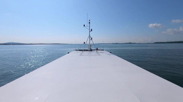 Ultra slow-motion 30fps front view of a ship cruising through calm waters, capturing the minimalist aesthetic of the vessel and a distant industrial skyline.