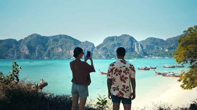 Young couple in Koh Phi Phi in Thailand taking pictures of the beautiful landscape. Turquoise blue water.