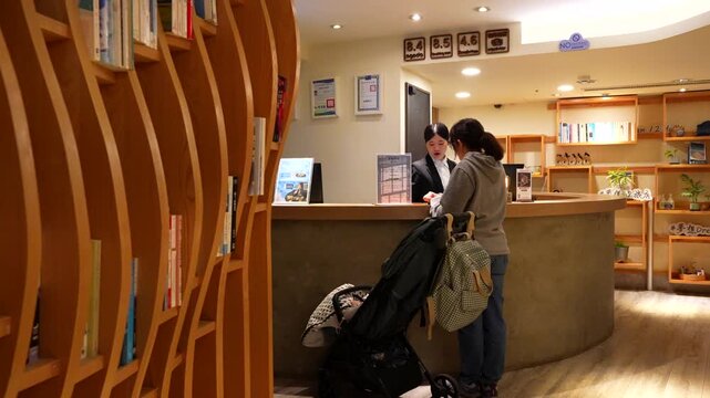 Young mother with a baby stroller checking in at a modern hotel lobby reception desk in Taiwan