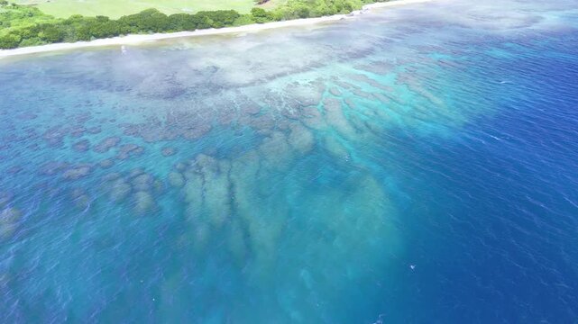 Top-down aerial drone movement showing the gradient from deep blue sea to intricate coral reef patterns near the shore.
