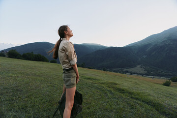 Obraz premium Cheerful woman outdoors, standing in a sunlit meadow with distant mountains, wearing casual shorts and shirt, enjoying fresh air, a peaceful moment, and a relaxed lifestyle