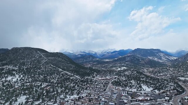 Estes Park rolling hills and forest with snow covered mountain ridge in background, aerial drone overview