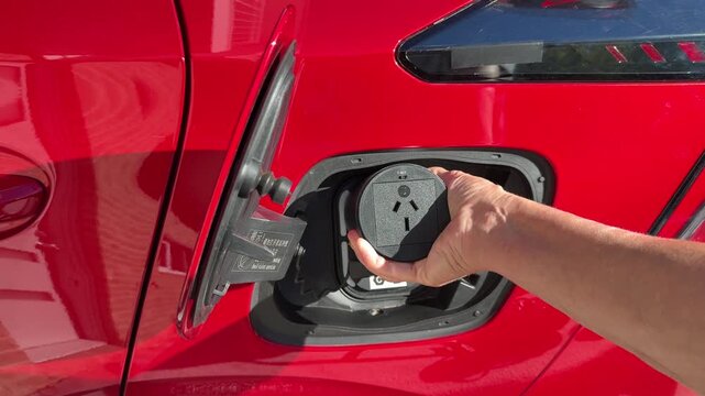 Close up of adapter plug for vehicle to load being un-plugged from a type 2 charge socket on a bright red electric car
