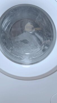 Closeup washing machine drum cleaning cycle with foam and rotating stainless interior