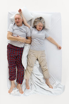 Senior couple sleeping on backs in relaxed positions on white bed. Concept of healthy sleep, mattress testing, bedroom essentials and comfort product promotion.