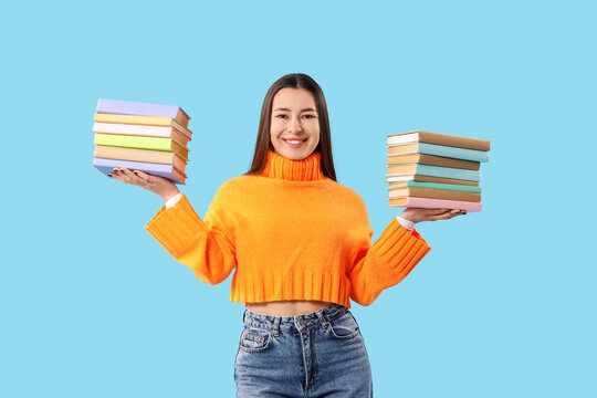 Beautiful young woman with stacks of books on blue background