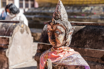 Naklejka premium Weathered female guardian figure stands within a sacred temple site surrounded by historic stone structures and cultural heritage architecture.