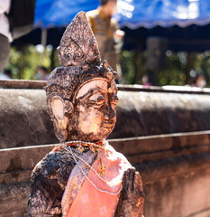 Naklejka premium Weathered female guardian figure stands within a sacred temple site surrounded by historic stone structures and cultural heritage architecture.