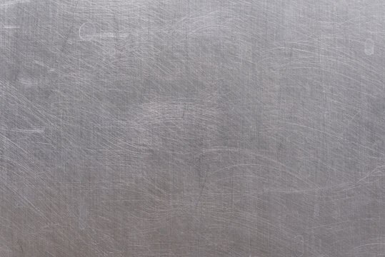 Close-up of scratched aluminum baking tray texture. Abstract metallic background with deep grooves and silver surface wear.