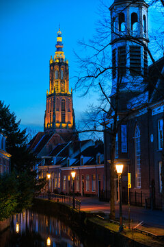 Dutch canal house with street lighting on, Onze Lieve Vrouwetoren clock tower in the background, Amersfoort, Netherlands, European lifestyle