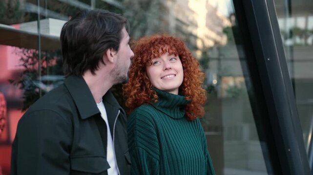 Caucasian man and woman with red curly hair talking and smiling together on a city street