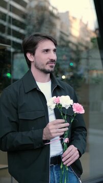 Handsome man with a bouquet of carnations waiting for his girlfriend on a city street