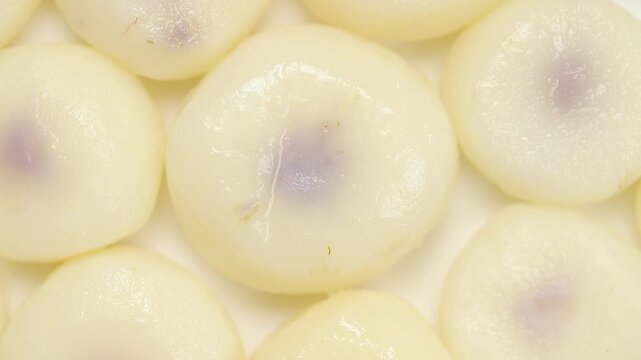 Slowly rotating boiled and peeled water chestnuts arranged on a white plate, Close-up view