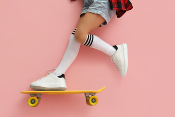 Legs of little girl with skateboard doing tricks on pink background © Pixel-Shot