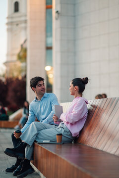 Young couple enjoying conversation on urban bench, drinking coffee in city square, developing business ideas