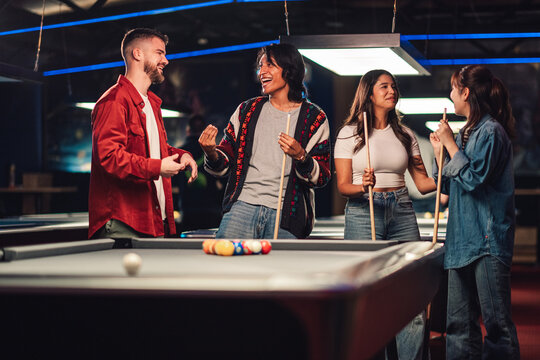 Diverse friends socializing and enjoying a game of billiards, celebrating success and teamwork in a modern pool hall