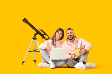 Fototapeta premium Young couple with laptop and telescope sitting on yellow background