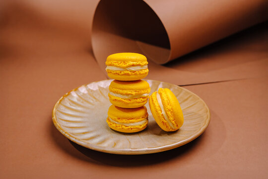 Yellow macarons stacked on a plate in a simple setup on a brown backdrop
