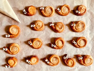 Cute snail shaped puff pastry cookies with candy eyes on baking paper © Penny Lin 