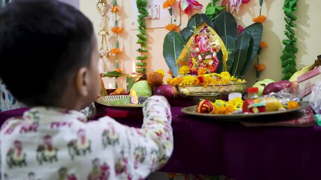 indian toddler worshiping ganpati bappa at decorated home temple during puja