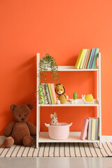 Naklejka premium Bookshelf with toys and plant near orange wall in children's room