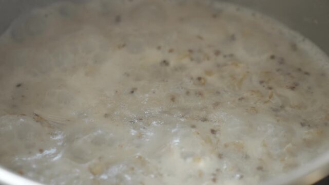 Closeup of boiling oatmeal porridge with bubbles and creamy texture. Concept of hot breakfast home cooking and meal preparation.