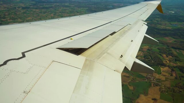Airplane turning while approaching landing with ailerons deployed. Jet banking above fields during descent with control surfaces activated. Aircraft maneuvering low over countryside as flaps extend
