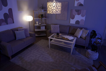 Interior of stylish living room with cozy sofas, coffee table and glowing lamps at night © Pixel-Shot