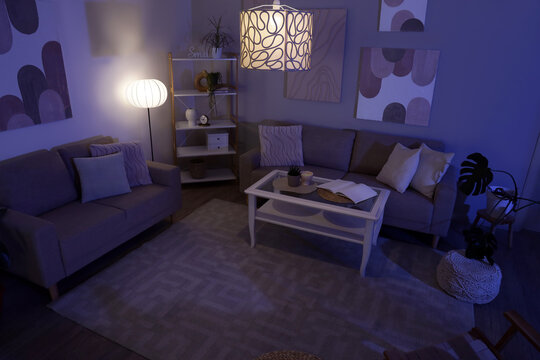 Interior of stylish living room with cozy sofas, coffee table and glowing lamps at night