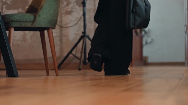 Closeup feet stepping across wooden floor, executive leaving meeting room with leather briefcase, tailored black trousers and polished loafers, confident brisk pace, chairs and studio light