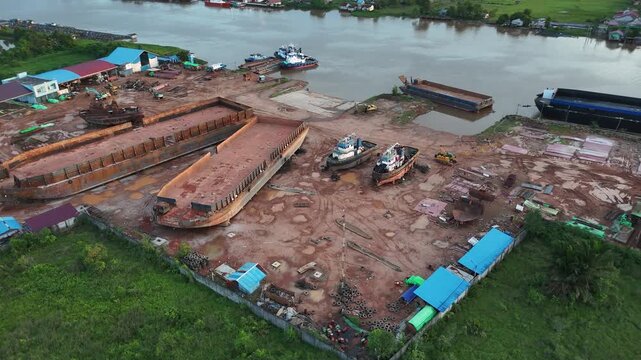 An aerial view of a river shipyard filled with barges, tugboats, and activity at an Indonesian industrial dock.