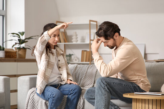 Unhappy man with his wife quarreling on sofa at home. Divorce concept