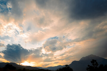 Obraz premium Clouds fill sky above mountain range during sunset. colors change as daylight fades. scene shows transition from day to night with dramatic light. Clouds gather in the sky, evening light