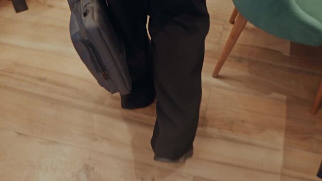 Legs walking hardwood floor business executive in suit carrying briefcase, measured stride across quiet lobby, polished shoes, shadow contrast, interior meeting approach, detailed floor texture