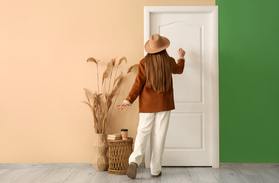 Young woman in autumn outfit standing knocking on door at home