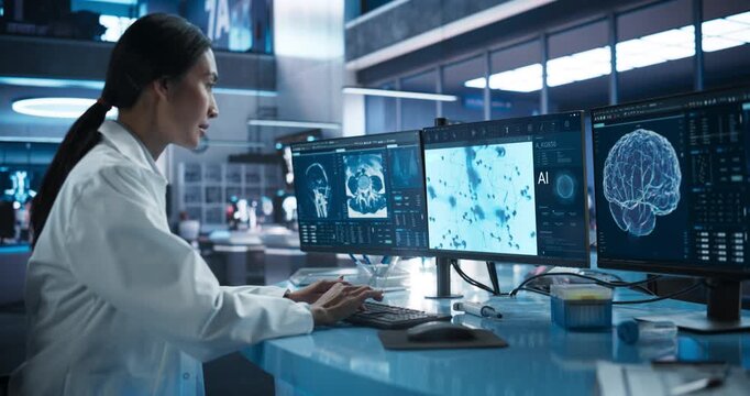 Asian Female Scientist Operates a Multi-monitor Workstation in a Clinical Lab, Analysing MRI, Neural and Cell AI Overlays for Diagnosis, Drug Discovery and Precision Cure. Moving Medium Side Angle.