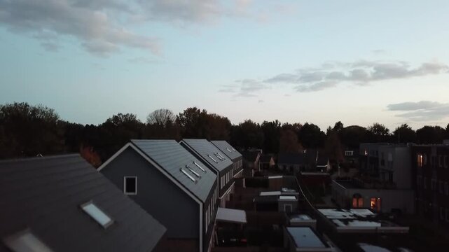 A captivating aerial drone video slowly descending over a quiet residential street during the evening hours, revealing rows of houses and back gardens bathed in the soft light of dusk. Scattered light