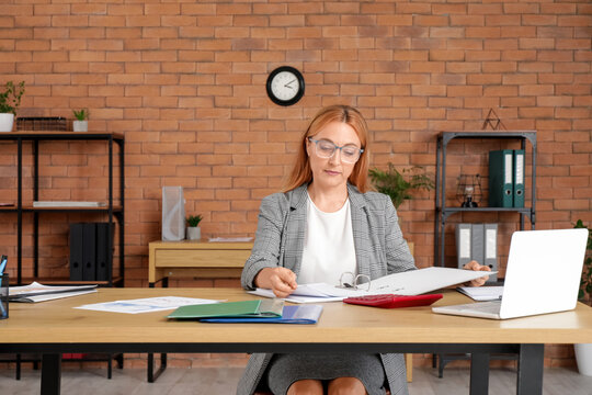 Female accountant in eyeglasses working with folder at workplace in office