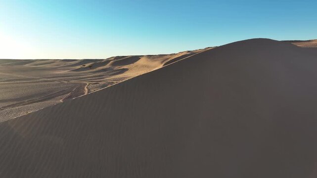 Aerial drone footage flying along sand dune crest with golden morning light and deep blue sky, Sahara desert Morocco