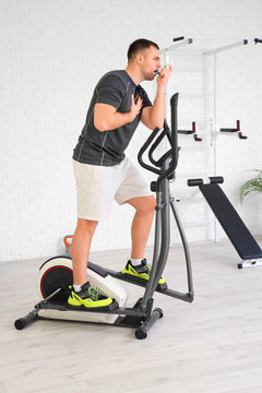 Sporty young man using inhaler on exercise bike in gym