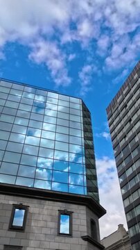 Clouds reflecting in glass office buildings against blue sky, modern urban architecture with mirrored windows and skyscrapers in city center, business district facade with cloud reflection and