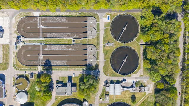 Aerial view of RWZI Echten wastewater treatment plant with circular aeration tanks and rectangular basins surrounded by lush green trees in Hoogeveen, Drenthe, Netherlands.