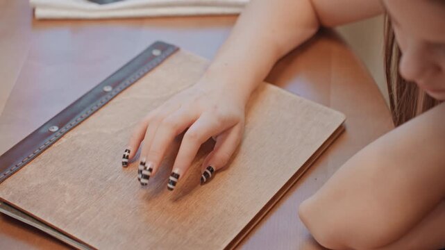 Closeup female hand on journal cover, textured leather binder, striped nails resting on pages, afternoon sunlight, contemplative writing pause, creative reflection and sketching ideas