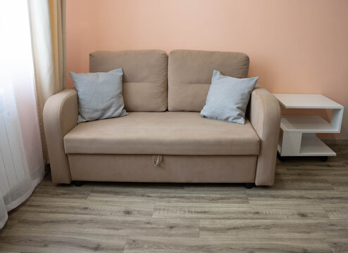 In the room, a beige sofa with pillows and a white nightstand is placed against the pink wall