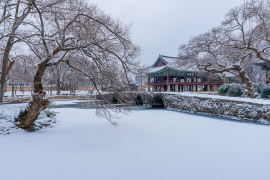 Traditional wooden structure of Gwanghallu Pavilion covered in white winter snow standing beautifully on a frozen pond under an overcast sky in Namwon.