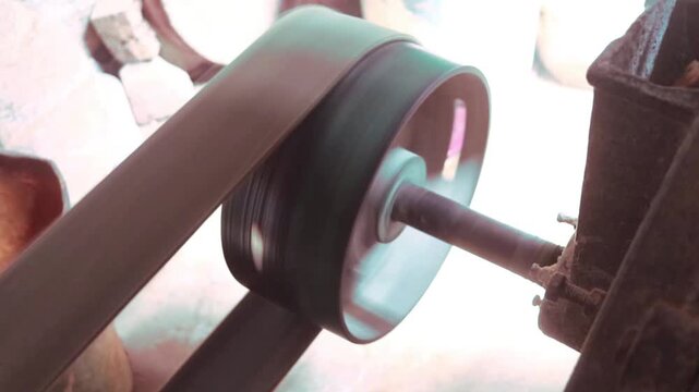 Rotating metal pulley wheel powered by a heavy rubber belt in a mechanical workshop setting