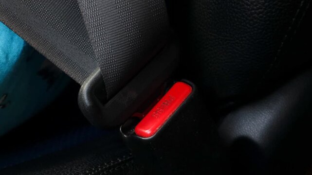 Close up of hand pressing car seat belt release button to unbuckle safety belt inside vehicle.
