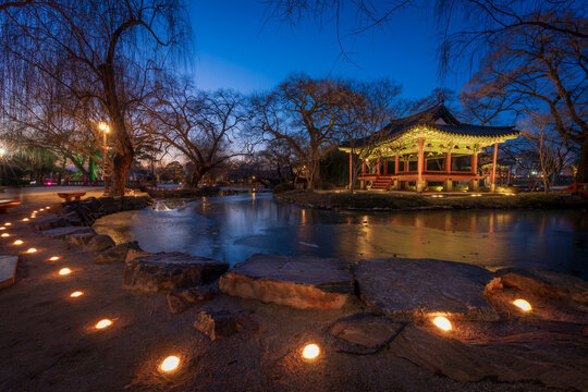 Serene twilight view of the illuminated Gwanghallu Pavilion overlooking a calm pond surrounded by bare winter trees and glowing ground lanterns in Namwon.